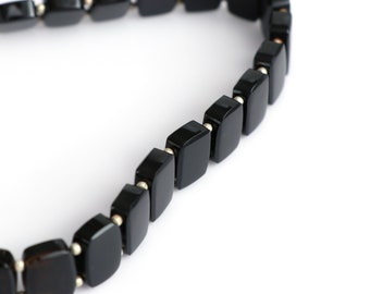 May include: A black necklace featuring rectangular onyx beads, each linked by small, silver-toned metal connectors. The polished beads create a sleek appearance. The necklace is set against a white backdrop, emphasizing its dark hue and minimalist style.