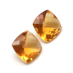May include: Two cushion-cut topaz gemstones, one on top of the other, with a golden yellow colour.