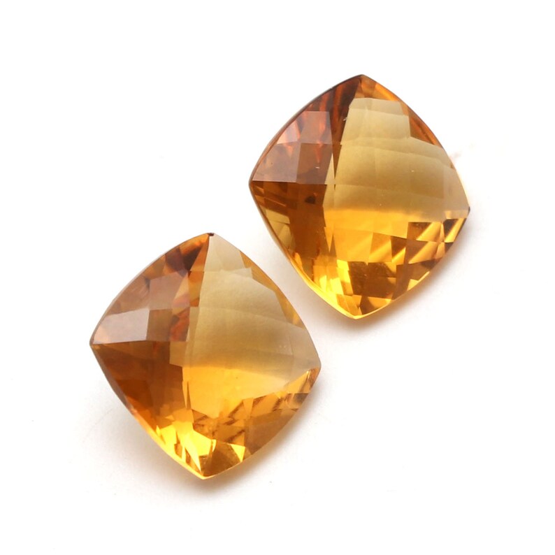 May include: Two cushion-cut topaz gemstones, one on top of the other, with a golden yellow colour.