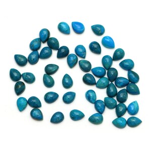 May include: A collection of teal blue gemstone cabochons in a teardrop shape. The stones are scattered on a white background.