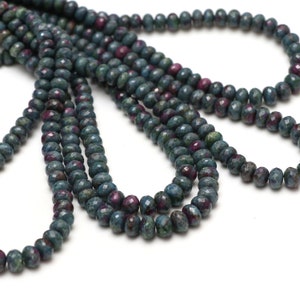 Może przedstawiać: Sznur ciemnozielonych i czerwonych koralików rubinowych. Koraliki są fasetowane i mają lekko nieregularny kształt.