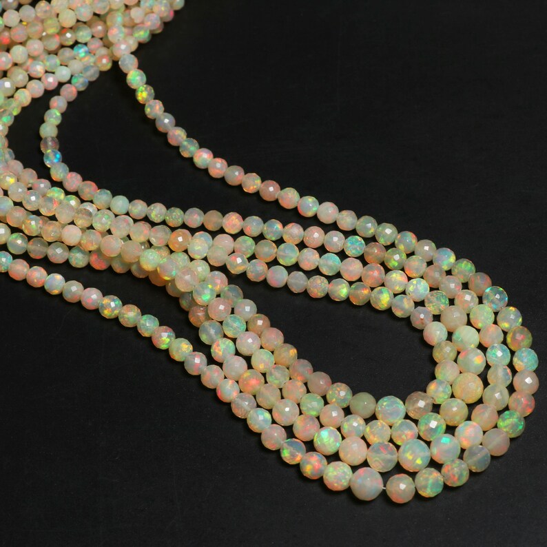 May include: A strand of iridescent white opal beads, each bead is faceted and has a slightly different color variation. The beads are strung on a clear thread and are arranged in a loose, flowing pattern.