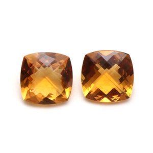 May include: Two cushion-cut citrine gemstones, each with a warm, golden-amber hue. The stones are faceted and have a high degree of brilliance.