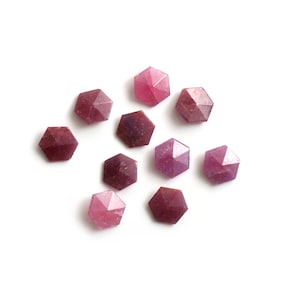 May include: Ten faceted pink gemstone beads, each with a star-shaped design, arranged in a scattered pattern on a white background.