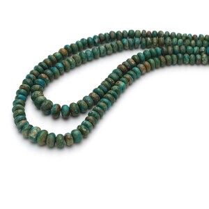 Op de afbeelding: Een streng groene turquoise kralen, met een gemarmerd patroon, wordt getoond in een close-up afbeelding. De kralen zijn rond en hebben een gladde, gepolijste afwerking.