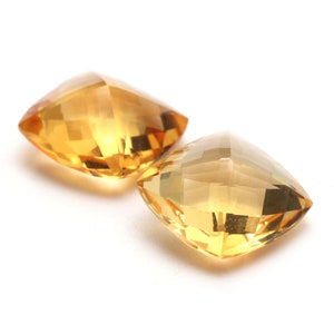 May include: Two golden yellow, faceted, square-shaped gemstones.