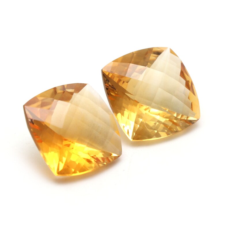 May include: Two cushion-cut topaz gemstones, one is a lighter yellow and the other is a darker yellow.