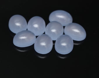 Puede incluir: Una colección de ocho piedras preciosas cabujón de color azul pálido, de forma ovalada y de lágrima, dispuestas sobre una superficie negra reflectante. Las piedras lisas y pulidas tienen un aspecto suave y translúcido, lo que sugiere que son calcedonia o un material similar.
