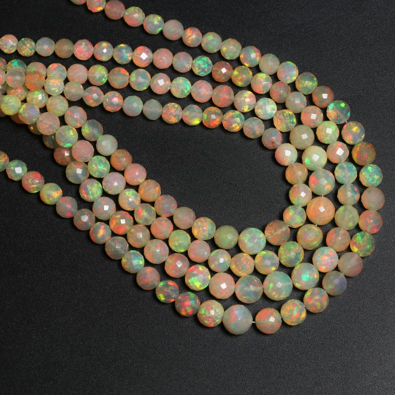 May include: A strand of iridescent opal beads, featuring a mix of light green, peach, and white colors. The beads are faceted and have a round shape.