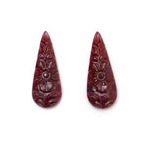 Puede incluir: Dos colgantes de piedra preciosa de color rojo rubí tallados en forma de lágrima con un diseño floral.