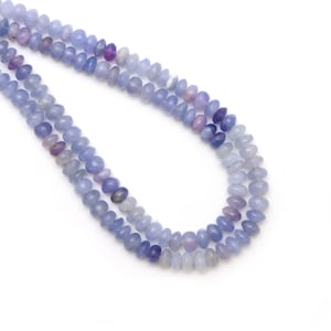 May include: A strand of blue gemstone beads. The beads are oval shaped and have a gradient of color from light blue to dark blue.