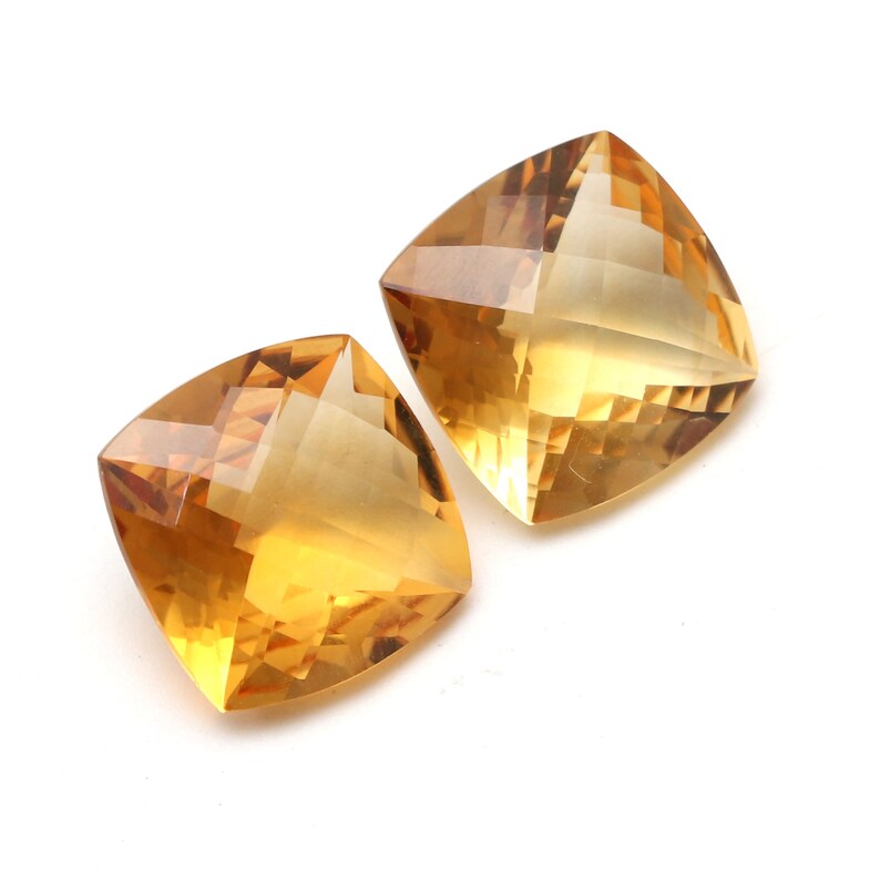 May include: Two square-shaped, faceted, topaz gemstones. The gemstones are a light to medium yellow colour.