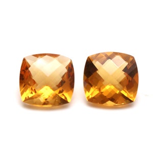 May include: Two cushion-cut, orange citrine gemstones. The gemstones are faceted and have a bright, clear colour.