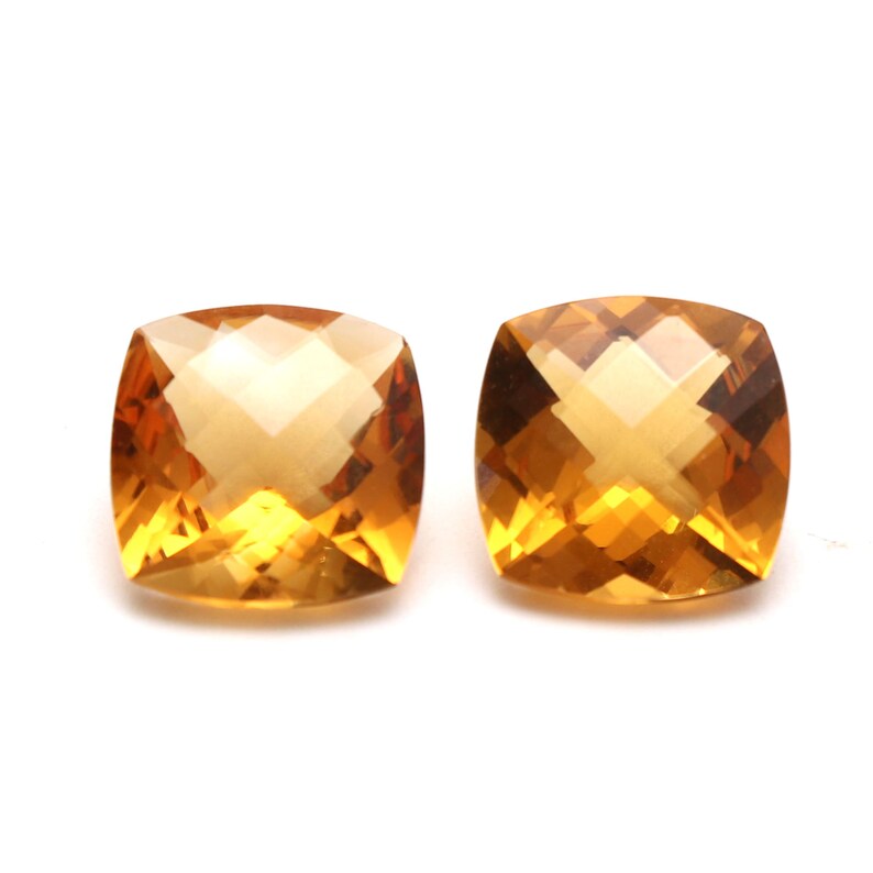 May include: Two cushion-cut, orange citrine gemstones. The gemstones are faceted and have a bright, clear colour.
