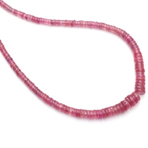 May include: A strand of pink gemstone beads, likely ruby, strung on a thin wire. The beads are faceted and have a slightly irregular shape.