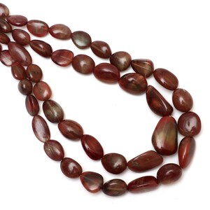 Puede incluir: Una hebra de cuentas de piedras preciosas de color marrón rojizo con forma ovalada lisa. Las cuentas están enhebradas en un hilo transparente y tienen un acabado natural y pulido.