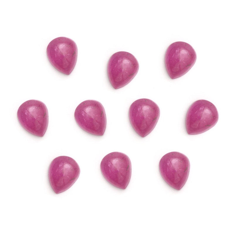 Puede incluir: Doce cabujones de color rosa en forma de l&aacute;grima, cada uno con un tono de rosa ligeramente diferente, est&aacute;n dispuestos en un patr&oacute;n disperso sobre un fondo blanco.