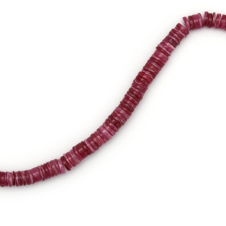 May include: A strand of pink and white shell beads, strung together to form a necklace. The beads are flat and round, with a slightly irregular shape.