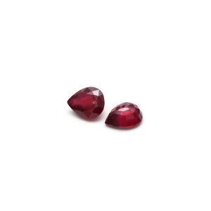 May include: Two pear-shaped red gemstones on a white background.