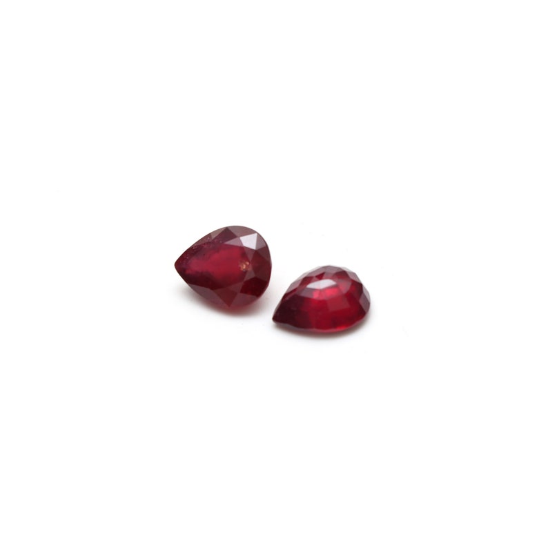 May include: Two pear-shaped red gemstones on a white background.