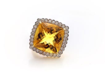 Pode incluir: Um anel de pedra preciosa amarelo-dourado de corte quadrado, com um halo de pequenas pedras preciosas transparentes. A cravação do anel parece ser dourada, e as pedras preciosas são colocadas sobre um fundo branco. O anel é uma joia.