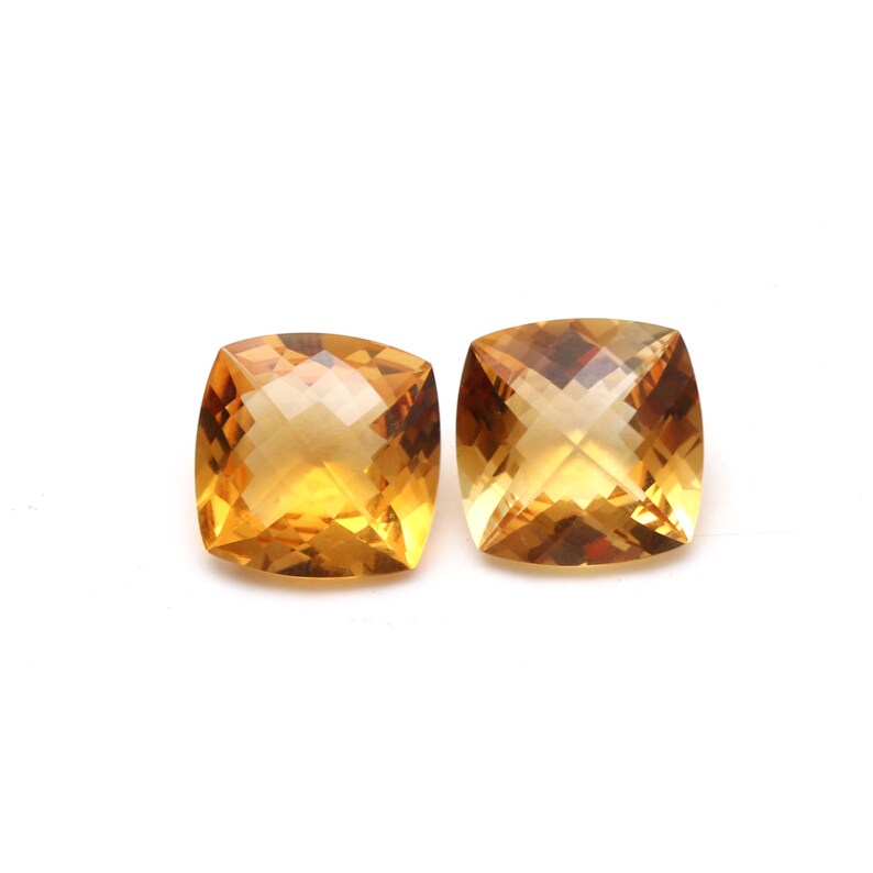May include: Two cushion-cut citrine gemstones, each with a golden yellow hue and a faceted surface.