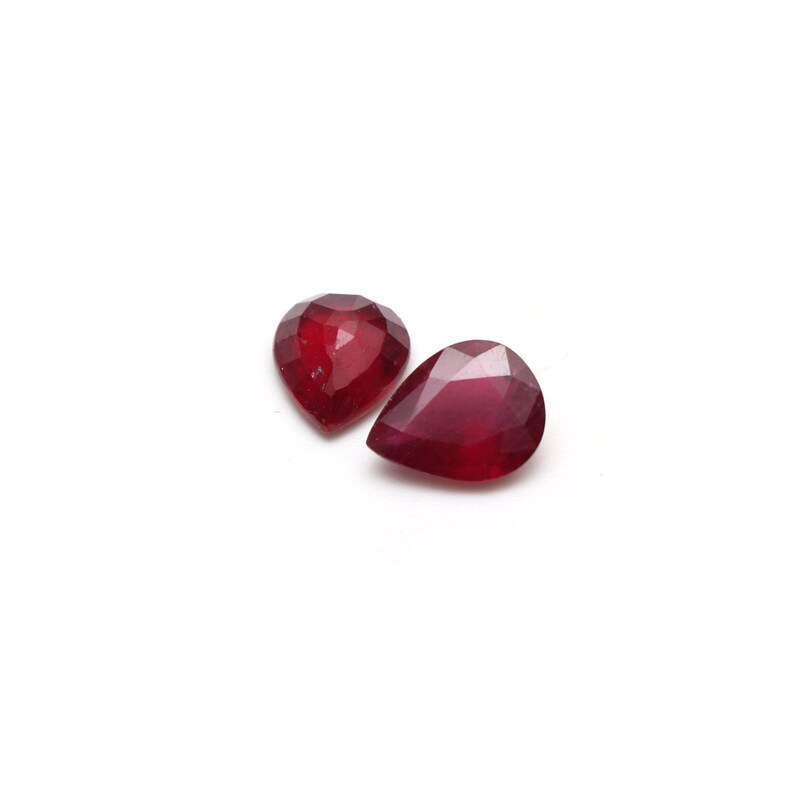 May include: Two pear-shaped red gemstones, likely rubies, are displayed on a white background.