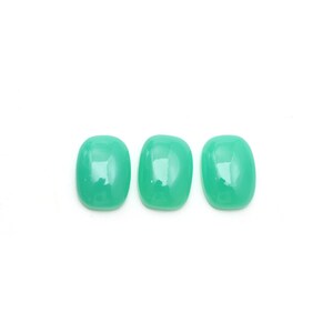 May include: Three polished, oval-shaped, light-green gemstones are arranged horizontally against a white background. The stones have a smooth, glossy surface, reflecting light. The gemstones are likely for jewelry making or collecting.