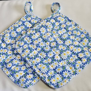 May include: Two blue and white quilted pot holders with daisy print and a loop for hanging.