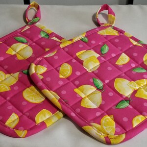 May include: Two pink quilted hot pads with a lemon print. The hot pads have a white polka dot background and yellow lemons with green leaves.