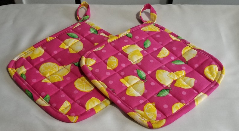 May include: Two pink quilted hot pads with a lemon print. The hot pads have a white polka dot background and yellow lemons with green leaves.