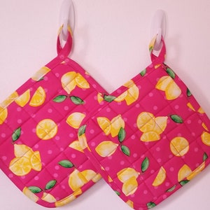May include: Two pink quilted hot pads with a lemon print and white polka dots. The hot pads have a loop for hanging.