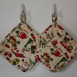 May include: Two quilted kitchen pot holders with a vintage design featuring red teapots, fruit, and kitchen appliances on a cream background.