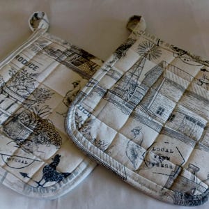 May include: Two quilted pot holders with a black and white farm scene design. One pot holder has the word "PRODUCE" printed on it. The other pot holder has the words "LOCAL FARM FRESH" printed on it. Both have a loop for hanging.