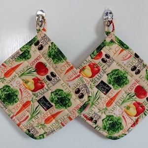 May include: Two beige pot holders with a quilted texture. The pot holders feature a colorful vegetable print with the words "Olive", "Lettuce", "Tomato", "Scallion", "Carrot", "Bell Pepper", and "Chili Pepper".