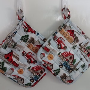 May include: Two quilted pot holders with a winter farm theme. The pot holders feature red trucks, barns, and trees on a white background.