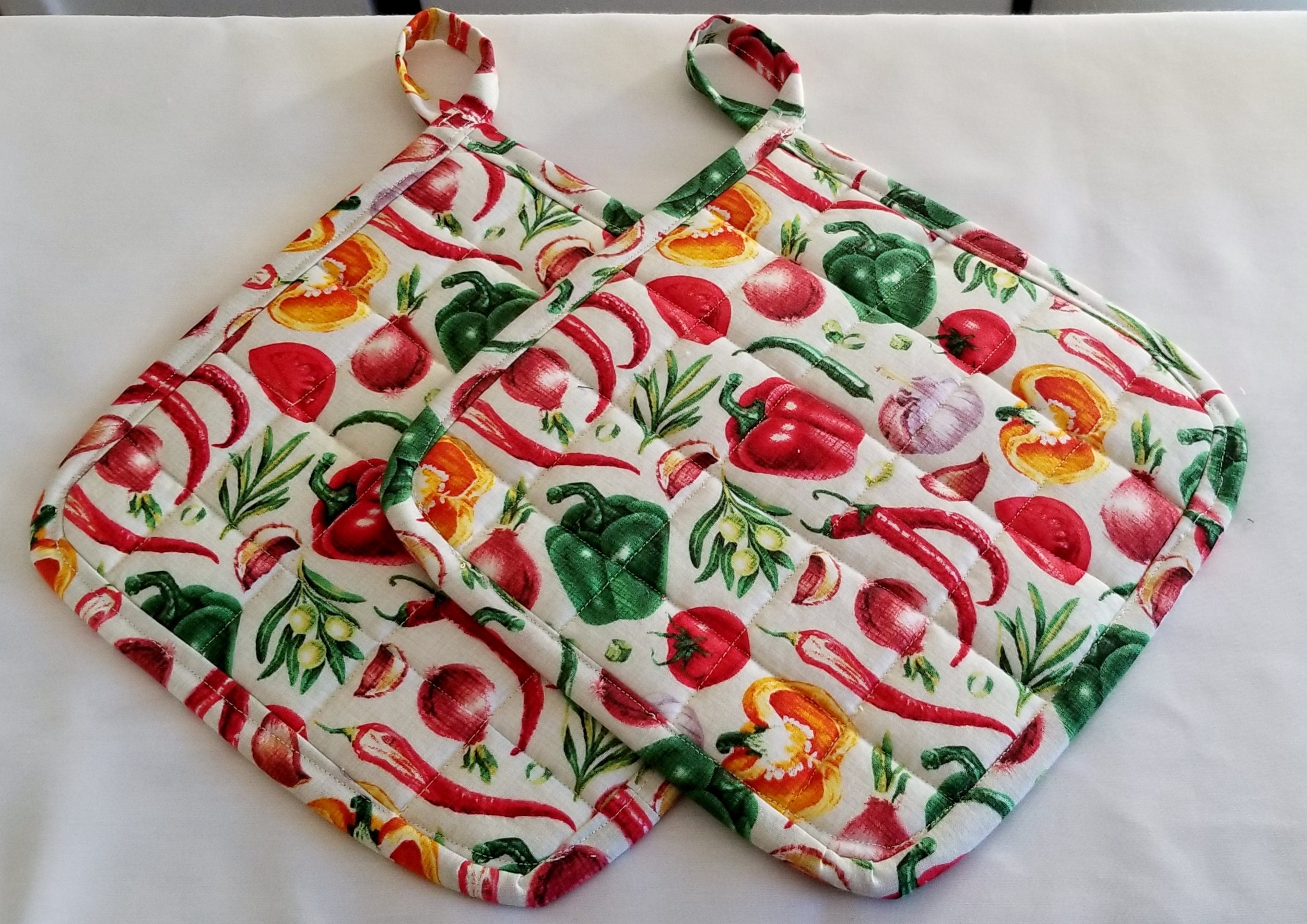 Two large handmade quilted pot holders or hot pads with a vegetable p…