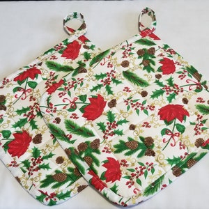 May include: Two white quilted pot holders with a Christmas-themed print featuring red poinsettias, green pine branches, brown pine cones, and gold accents.