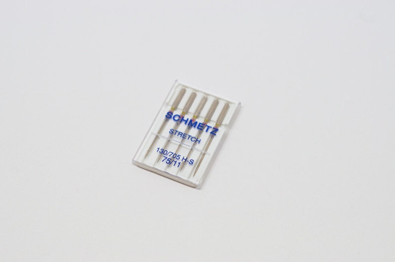 May include: A clear plastic package of four silver sewing machine needles labeled "SCHMETZ STRETCH 130/705 H-S 75/11"