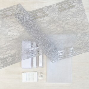 May include: A set of white lace fabric, white elastic, white bra strap adjusters, and silver bra hooks. The fabric is a delicate floral pattern.