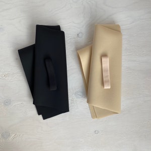 May include: Two pieces of fabric, one black and one beige, are folded and laid out on a white surface. A black elastic band is attached to the black fabric.