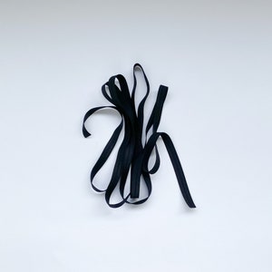 May include: A close-up of black elastic ribbon, folded and twisted, against a white background.