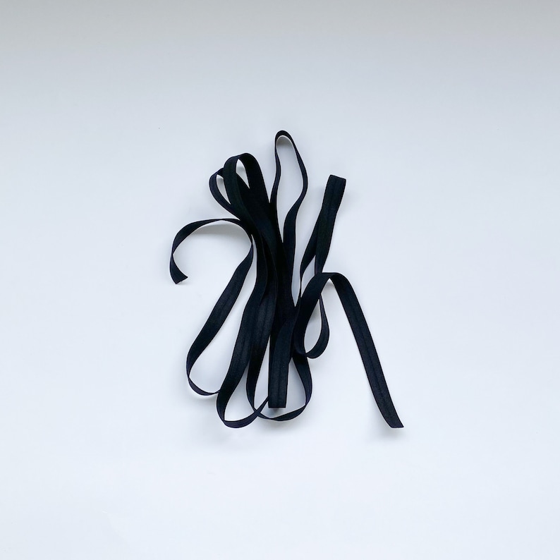 May include: A close-up of black elastic ribbon, folded and twisted, against a white background.