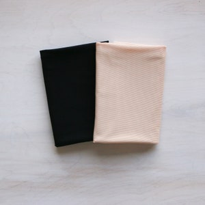 May include: Two fabric swatches, one black and one light beige, are laid out side by side on a white surface.