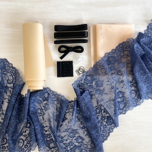May include: A collection of lingerie-making supplies, including navy blue lace trim, beige fabric, black elastic bands, a bow, bra hooks, and a ring. The materials are arranged on a light-colored surface, showcasing the components for crafting intimate apparel.