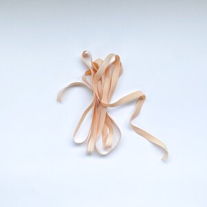 May include: A close-up of a bundle of light brown, wooden ribbon. The ribbon is twisted and knotted, creating a natural and rustic look.