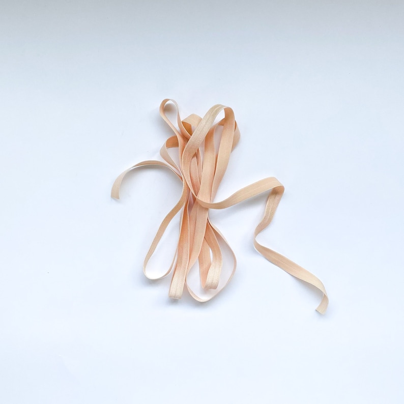 May include: A close-up of a bundle of light brown, wooden ribbon. The ribbon is twisted and knotted, creating a natural and rustic look.