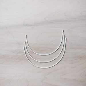 May include: Three white metal hoops of different sizes, nested together, on a light wood surface.