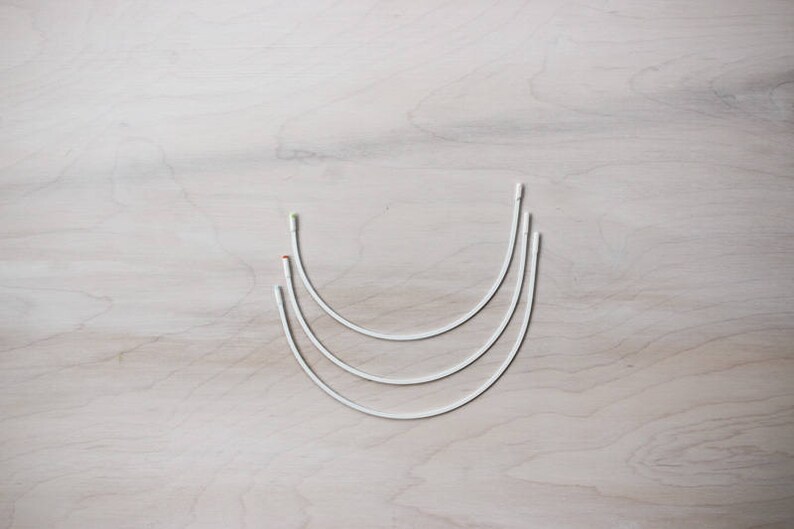 May include: Three white metal hoops of different sizes, nested together, on a light wood surface.