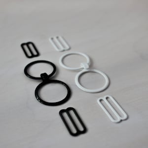 May include: Two sets of black and white metal bra strap adjusters. Each set includes two rings and a slider.